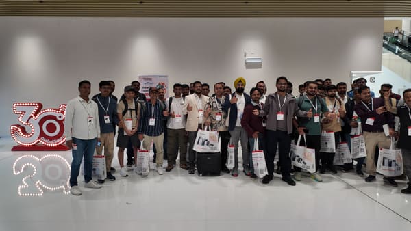 Group of men from India at a Global Sources trade fair, holding bags and smiling.