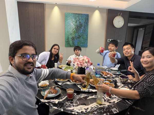 A group of seven people, including adults and children, dining and toasting at a table with food and drinks.