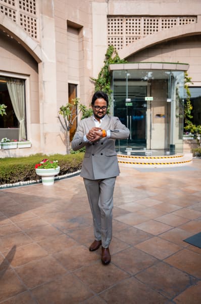 Man in a grey suit and glasses checking his orange smartwatch outside a modern building.