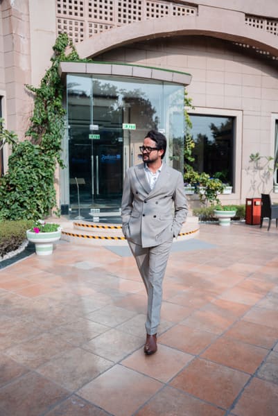 A man in a light grey suit and glasses walks confidently outside a Radisson hotel entrance on a sunny day.