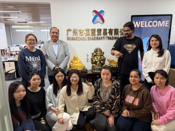 A diverse group of eleven people, including men and women, smiling in an office with a company logo and welcome screen.
